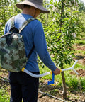 Person using Backpack Style Handheld Manure Spreader For Garden And Field Work, durable Oxford and PVC construction, outdoors