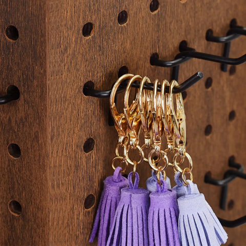 Rotating Wooden Jewelry Display Stand With Four Sided Pegboard And 48 Removable Black Hooks To Flex Your Earring And Accessory Collection On A Warm Brown Base featuring gold clips and purple tassels.