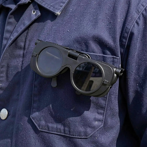 Premium Heavy Duty Industrial Double Lens Welding Goggles resting on a work uniform pocket, featuring dark lenses for glare reduction.