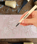 Hand carving design on a linoleum block with wood tools, part of an Eight Piece 4x6 Inch Linoleum Carving Blocks For Printmaking And Rubber Linocut Stamps Kit With Wood Carving Tools And Brayer Roller For DIY Crafts.