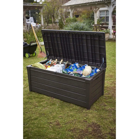 Lockable 120 Gallon Outdoor Storage Deck Box in brown with lid open, showing cushions, tools, and pool toys in garden setting