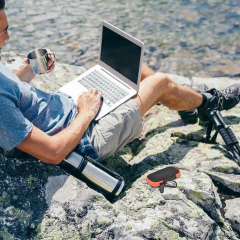 Man using laptop outdoors with Hard Case For SanDisk Extreme Portable SSD Built Tough Rugged Foam Padding And Mesh Pocket For USB Cables And SD Cards Custom Fit External Drive Protector In Bright Orange Zipper.
