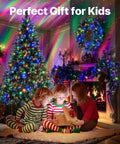 Children in pajamas gazing at a gift with Epic Galaxy Projector Star Light illuminating a Christmas scene with a tree and fireplace.