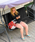 Person sitting on a two-seat patio swing with No Fuss All Weather 600D Oxford Swing Seat Cover Replacement For Two To Three Seat Patio Garden Chairs Outdoor Bench Waterproof Coffee XXL 58.3 By 19.7 By 19.7 Inches.