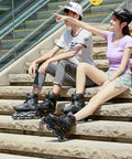 Two people wearing adjustable inline skates for beginners, sitting on stairs outdoors, showing black skates with triple closure buckle straps.
