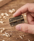 Small Antique Cabinet Hinges With Rounded Corners Four Hole Vertical Iron Construction in hand on wood surface