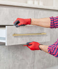 Person installing No Nonsense Solid Brass Cabinet Pulls With Sleek Brushed Gold Finish on a gray drawer front.