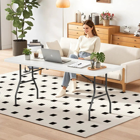 Woman working at Six Foot Folding Table For Indoor And Outdoor Use Portable Picnic Party Table With Carrying Handle Fold In Half Design Lightweight White Plastic Perfect For Parties BBQs Weddings Camping And More in a cozy living room setting.