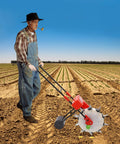 Farmer using Hand Push Garden Seeder Roller Planter for Easy Seed Drop in field with vast rows of crops under blue sky