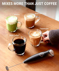 Handheld Milk Frother Wand With 2 Whisks, Electric Coffee Mixer For Creamy Foam, One-Press Operation next to various drinks on table.