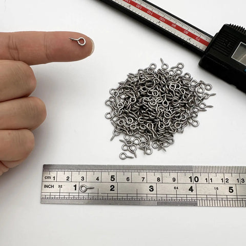 Tough As Nails Premium 304 Stainless Steel Screw Eye Hooks 5Mm By 10Mm displayed on a finger with measuring ruler for size reference.