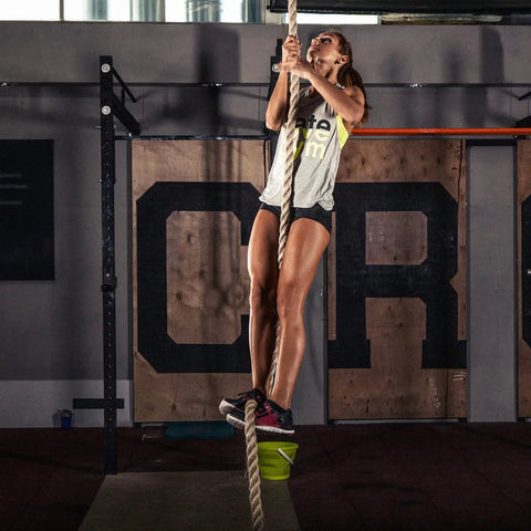 Woman climbing a rope in gym, showcasing athleticism, perfect for Built Like A Tank Wall And Ceiling Mount Bracket for Suspension Straps.