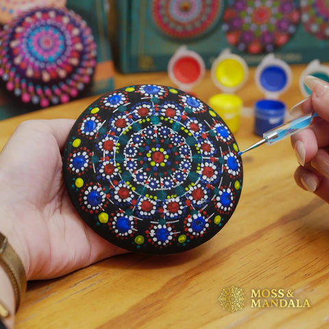 Person using Rock Painting Kit With Dotting Tools And Stencils And Acrylic Paints For Easy At Home Relaxing DIY Arts And Crafts Includes 5 Wooden Rocks 6 Mandala Stencils 12 Vibrant Colors And All The Dotting Tools For Adults And Women to paint a wooden rock with mandala design