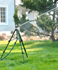 Heavy Duty Zinc Tripod Base Impact Sprinkler, 360 Degree Rotating, 3 Height Adjustable Steel Sprinkler Head, A Workhorse For Large Yards, Farms, And Garden Beds in operation on a lawn near a house, spraying water.