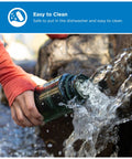 Hand pouring water from a Rugged 32 Oz Wide Mouth Reusable Water Bottle With Tight Seal Black Lid outdoors.