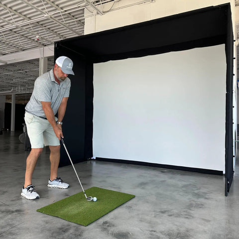 Golfer using Complete Golf Practice Backdrop Enclosure Gear With Poles Corner Connectors Side And Top Netting Impact Screen And Carry Bag For A 10 Feet By 8 Feet Indoor Home Golf Setup in a warehouse setting
