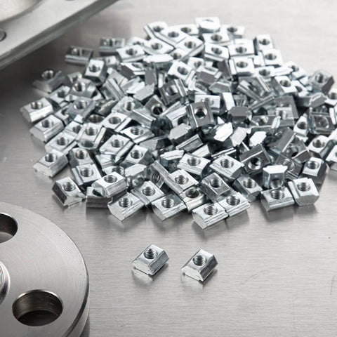 M4 Sliding T Slot Nuts 200 Pack For 2020 Aluminum Extrusion Profiles scattered on a metallic surface, showing their heavy-duty design.