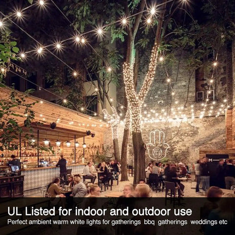 Globe Outdoor String Lights 29Ft With 15 Dimmable Plastic Bulbs illuminating a busy outdoor cafe setting at night.
