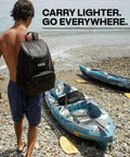 Man with black backpack by blue kayaks on beach, focus on lightweight 15 can backpack cooler insulated bag olive green for men and women