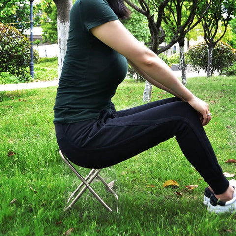 Person sitting on Portable Oxford Cloth Folding Stool With Lightweight Aluminum Frame in a garden setting