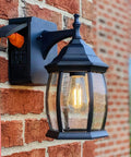 Traditional Outdoor Wall Sconce With Seeded Glass And Two Built In GFCI Outlets For Easy Access Power Black Finish Weather Resistant Porch Lighting For Patio Or Garden mounted on brick wall.