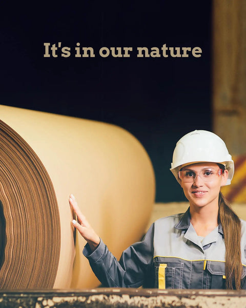 Woman in safety gear touching large roll of paper in manufacturing setting, showcasing industrial work environment.