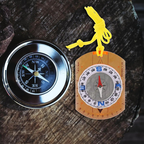 Rugged Orange Orienteering Hiking Compass With Lanyard For Hiking Camping And Backpacking next to a metal compass on a wooden surface