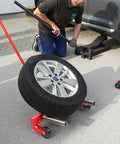 Man using Heavy Duty Adjustable Tire Wheel Dolly Full Size Cart Rock Solid 660 Lbs Capacity for tire removal in garage.