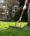 19 Tine Cold Pressed Steel Dethatcher Rake With 72 Inch Adjustable Handle in use on lawn near greenhouse