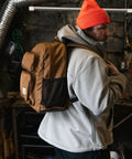 Man wearing 27L Single Compartment Laptop Backpack With Durable Duravax Base Rain Defender Water Repellent 1200 Denier Polyester Built For The Daily Grind On The Go For Work School Or Travel Laptop Sleeve Included, in a workshop setting.