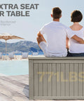Rear view of two people sitting on a Beefy 220 Gallon Outdoor Deck Storage Box With Removable Divider by pool, light brown.