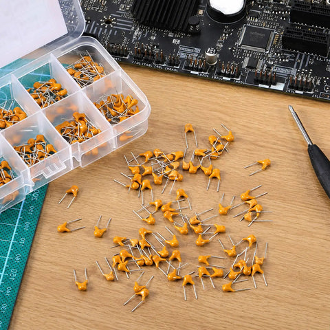 Sweet Ceramic Capacitor Assortment Kit Featuring Ten Darn Reliable Microfarad Values Perfect For Quick Circuit Fixes Hella Versatile Electronics Hobbyist Gear With Sturdy Tote Box Inside, showcasing capacitors spread out on a workbench.