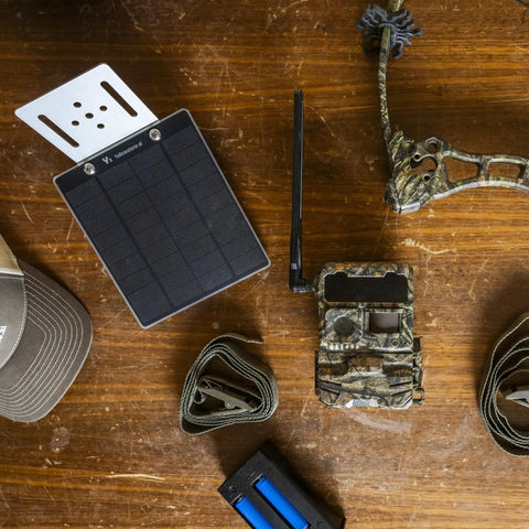 All Day Energy Boost Solar Panel For Y2 Cellular Trail Camera on wood surface with camo camera, straps, and cap.