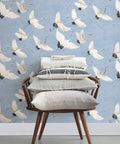 Chair with cushions in front of Windsong Crane Wallpaper Periwinkle, Unpasted Nonwoven, 10.4-Inch Repeat, Hand-Painted Crane Motif