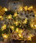 Bee String Lights 40 LED With Remote in yellow illumination, entangled with white flowers, perfect for decor use.