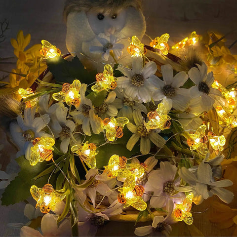 Bee String Lights 40 LED With Remote in yellow illumination, entangled with white flowers, perfect for decor use.