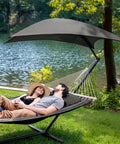 Standing Patio Hammock With Canopy And Foldable Stand, Portable And Easy Setup, Patent Pending, Dark Gray, Two Layer Quilted Polyester Comfort For Camping And Outdoor Kickback Lounging with couple relaxing by a lake.