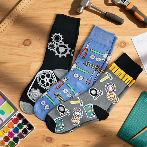 Three Pack Mechanical Engineering Socks Gift Set For Gearhead Men And Techy Dads with gear and tool prints on a wooden table.