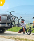 Man installing modular two in one hitch rack for two bikes up to eighty pounds on a truck with child observing, tilts and folds for storage, uses no frame contact, fits standard two inch hitches.