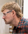 Kickass Rimless Wraparound Safety Glasses With Ultra Light Twenty One Gram Flex Plus Heavy Duty Dust Defense And Never Fog Tech For Top Shelf Eye Armor On Every Work Shift worn by a man in profile view.