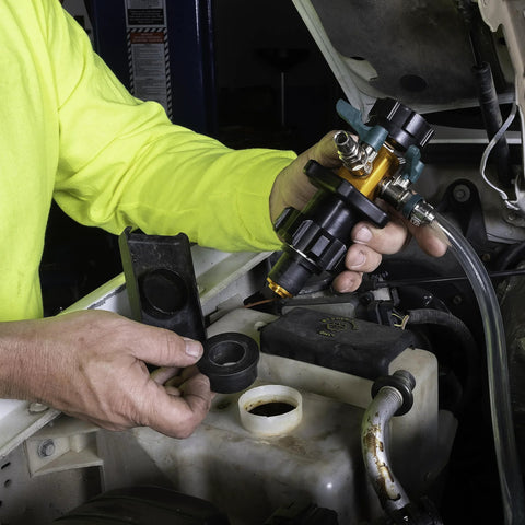 Front view of yellow and black cooling system refiller tool with hoses, held by mechanic near vehicle coolant reservoir.