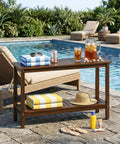 All Weather Patio Bar Table And Console With Two Shelves, 48 Inch Solid Wood Indoor Outdoor Multipurpose Buffet Storage Organizer, Espresso Finish, Adjustable Feet, Durable Outdoor Ready beside a pool with towels and drinks