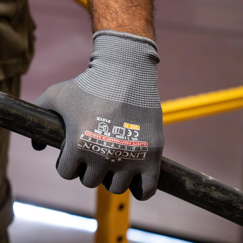 Close-up of a hand wearing grey knit wrist gloves holding a metal bar, showcasing 12 Pack Safety Performance Series Work Gloves For Construction And Mechanics Heavy Duty With Breathable Flex Superior Dexterity Knit Wrist Keeps Dirt Out Grey Size Large Durable Grip For Tools And Hand Protection.