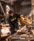 Man in workshop wearing Men's Carrier Hoodie Black Pullover Sweatshirt with Front Pockets, using saw for woodworking.