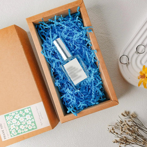 Top Shelf White Crinkle Paper Shreds And Gift Basket Filler cushioning a glass bottle in a brown box with blue shreds.