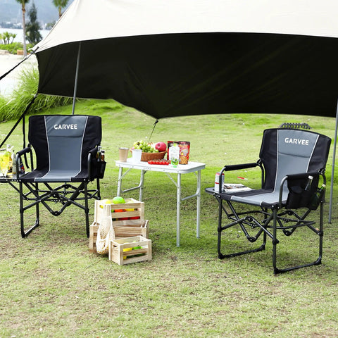 Two black Oversized Directors Camping Chairs With Side Table set up next to a picnic table outdoors on grass.