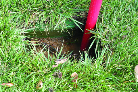 Siphon King 24 Inch Hand Transfer Pump With 36 Inch Hose in use, removing water from a grassy pit; visible red pump handle.