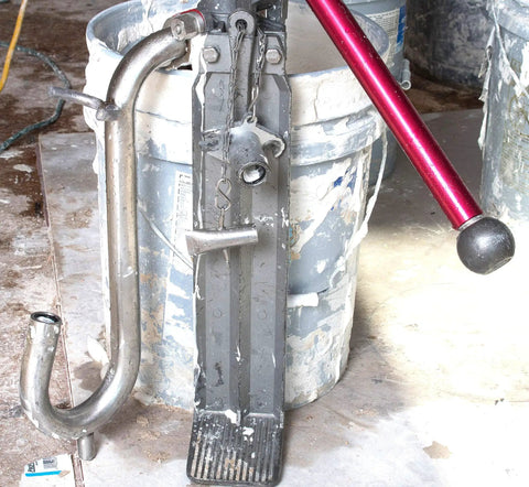 Pro Grade Compound Pump Gooseneck for Drywall Mud Loader, heavy-duty stainless steel next to mud bucket.
