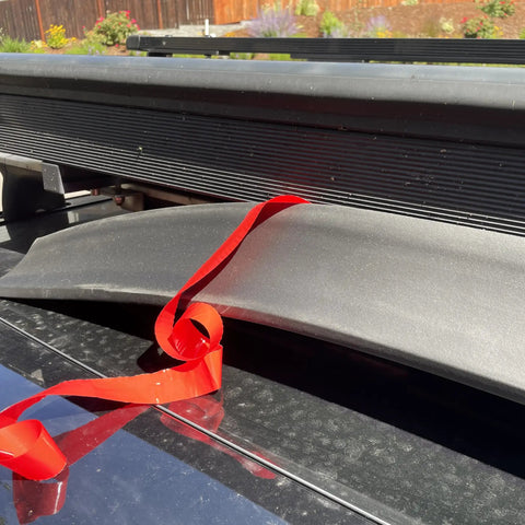 Premium Flexible Wind Deflector Fairing For Roof Rack Crossbars with foam rubber and red strap on vehicle roof.