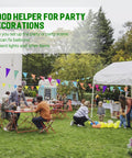 Outdoor garden party with people setting up decorations and arranging colorful balloons and bunting under tents and trees.